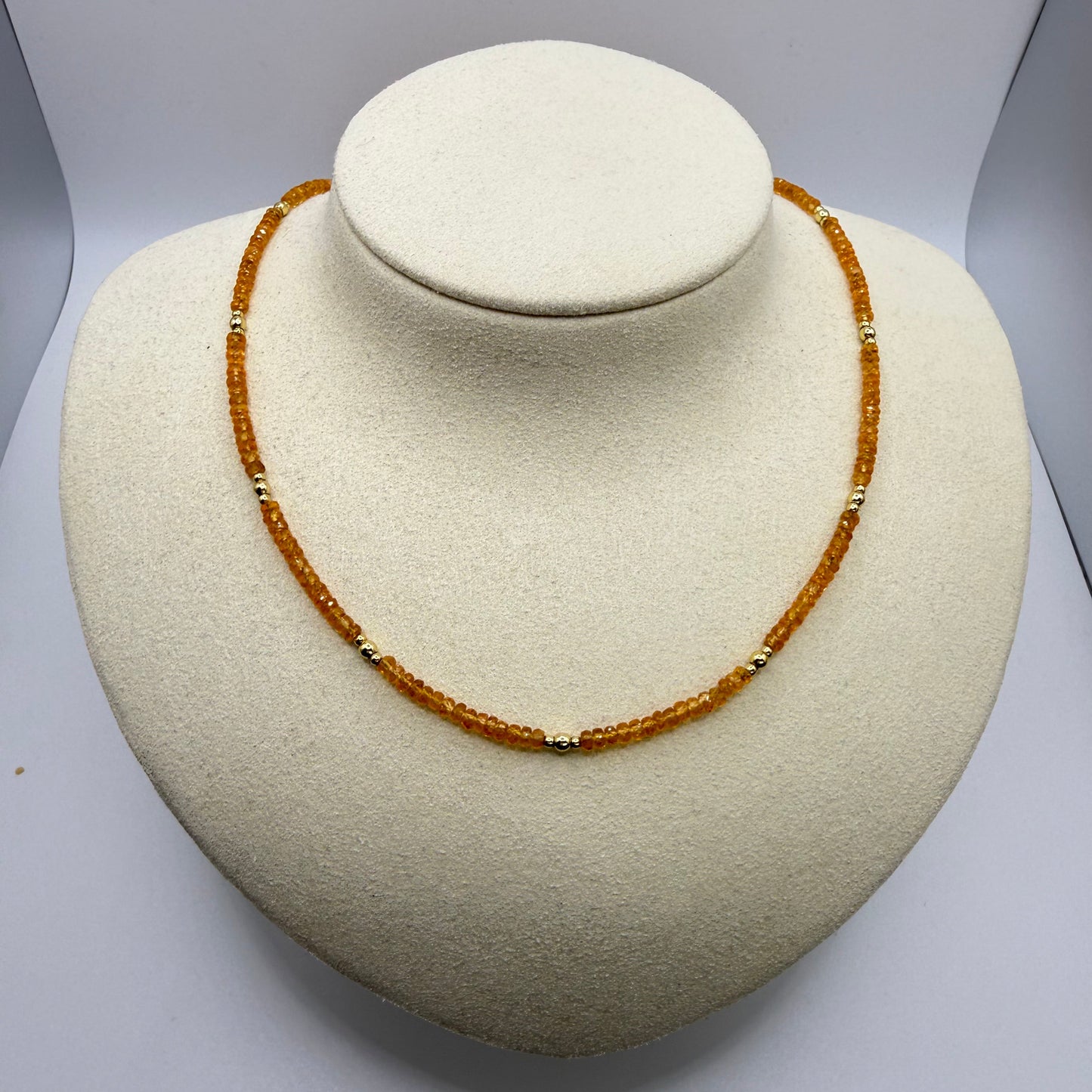 An orange gemstone necklace on a beige textured display bust.