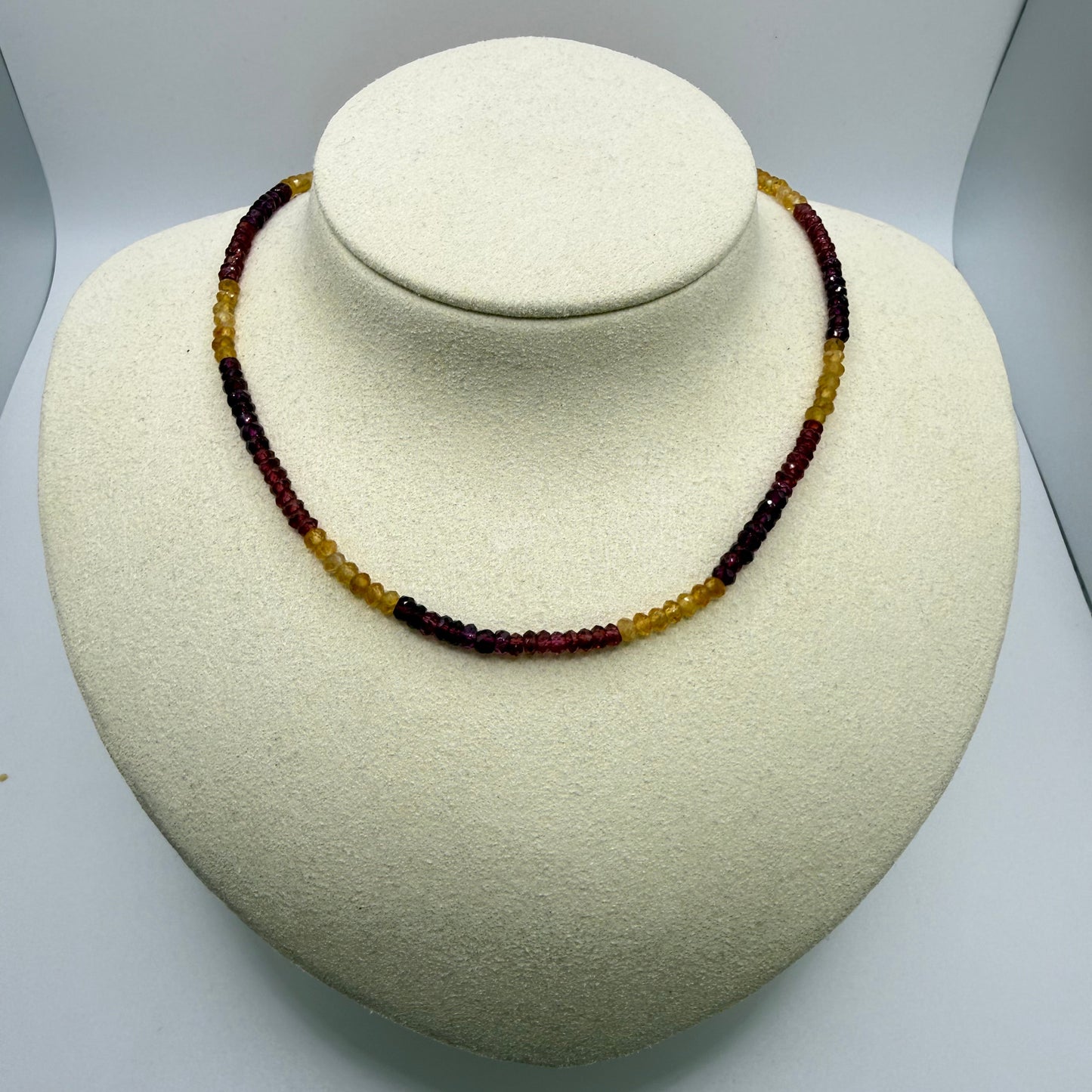 Dark purple and yellow beaded necklace on a white display bust.