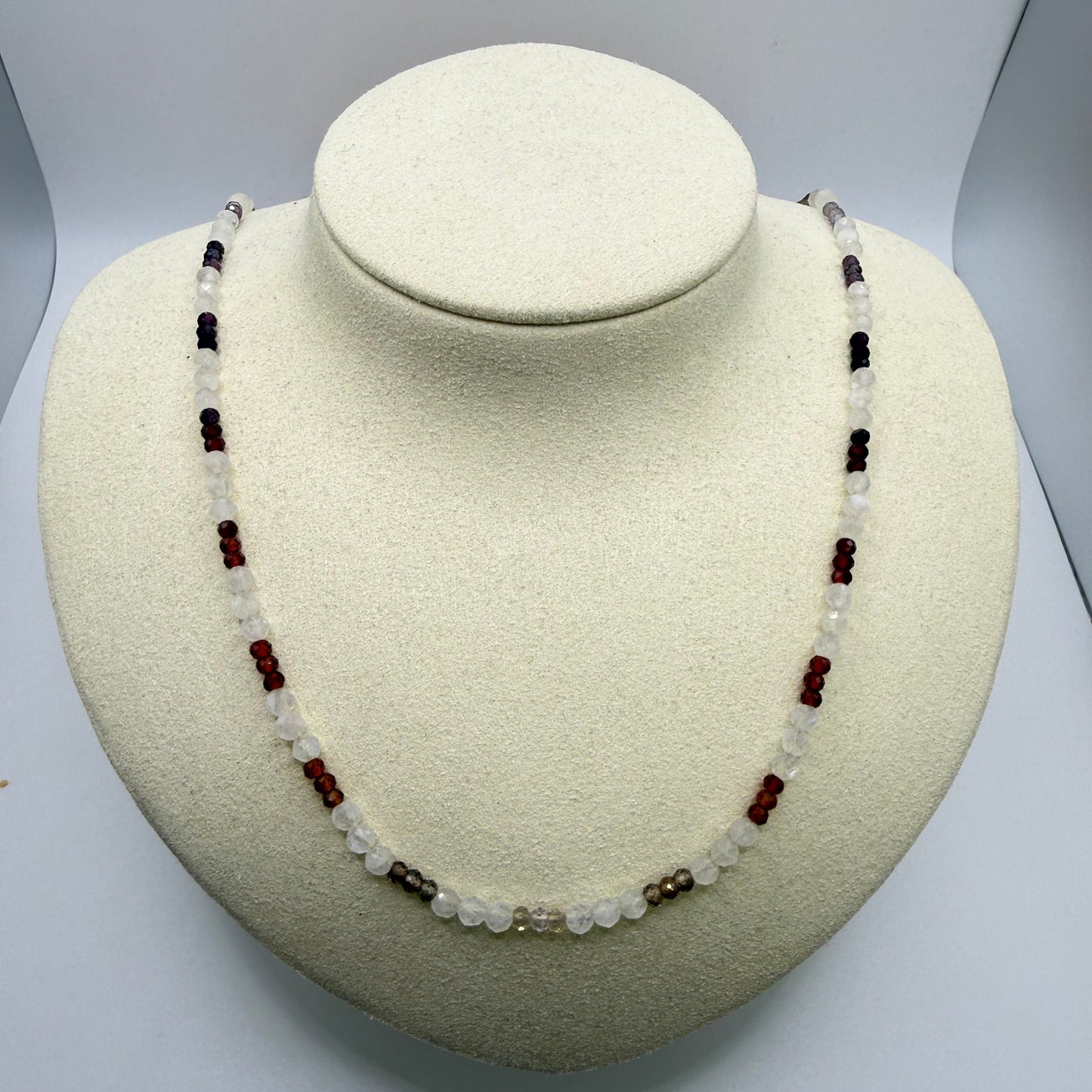 White and earth toned beaded necklace on a white display bust.