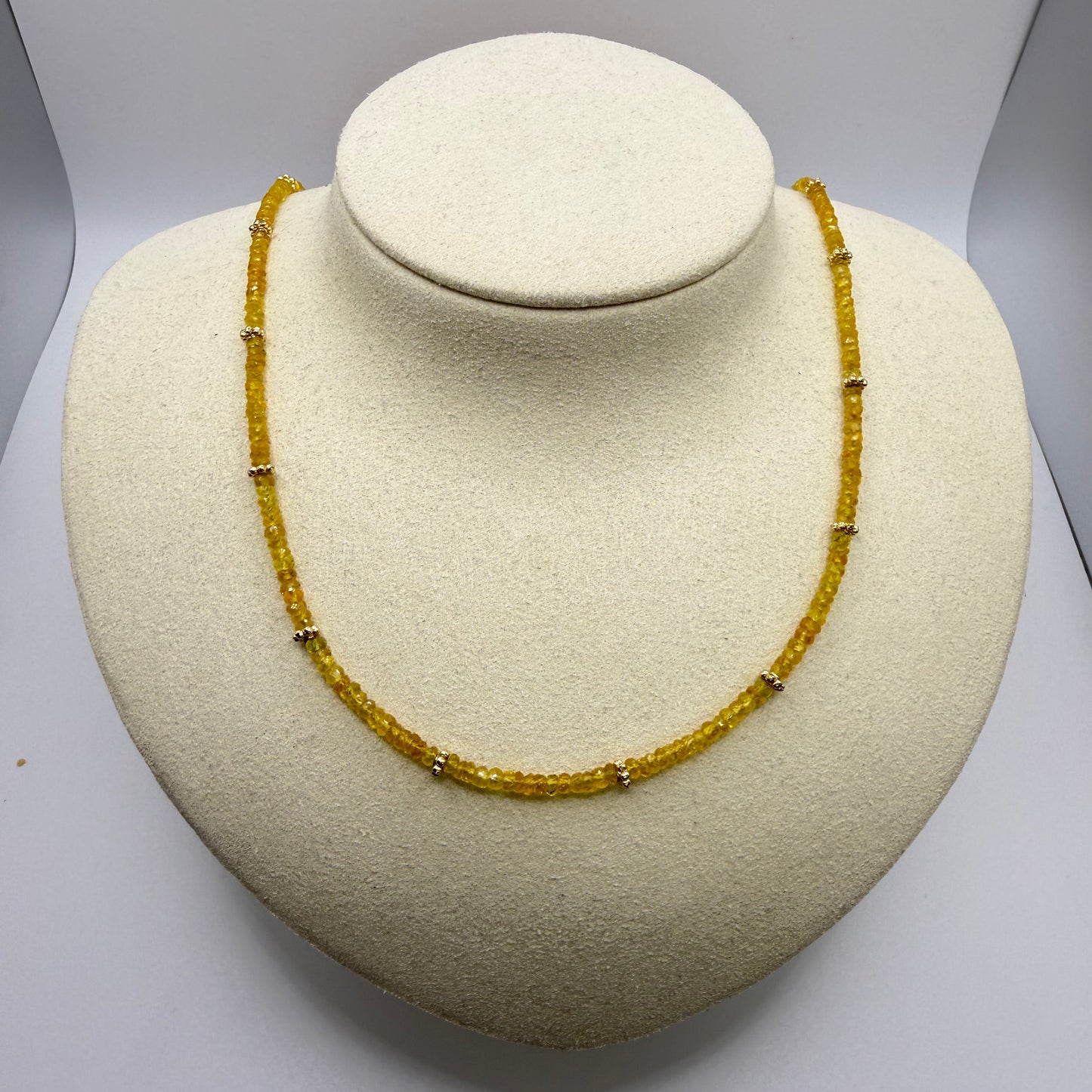 Yellow gemstone necklace on a beige textured display bust