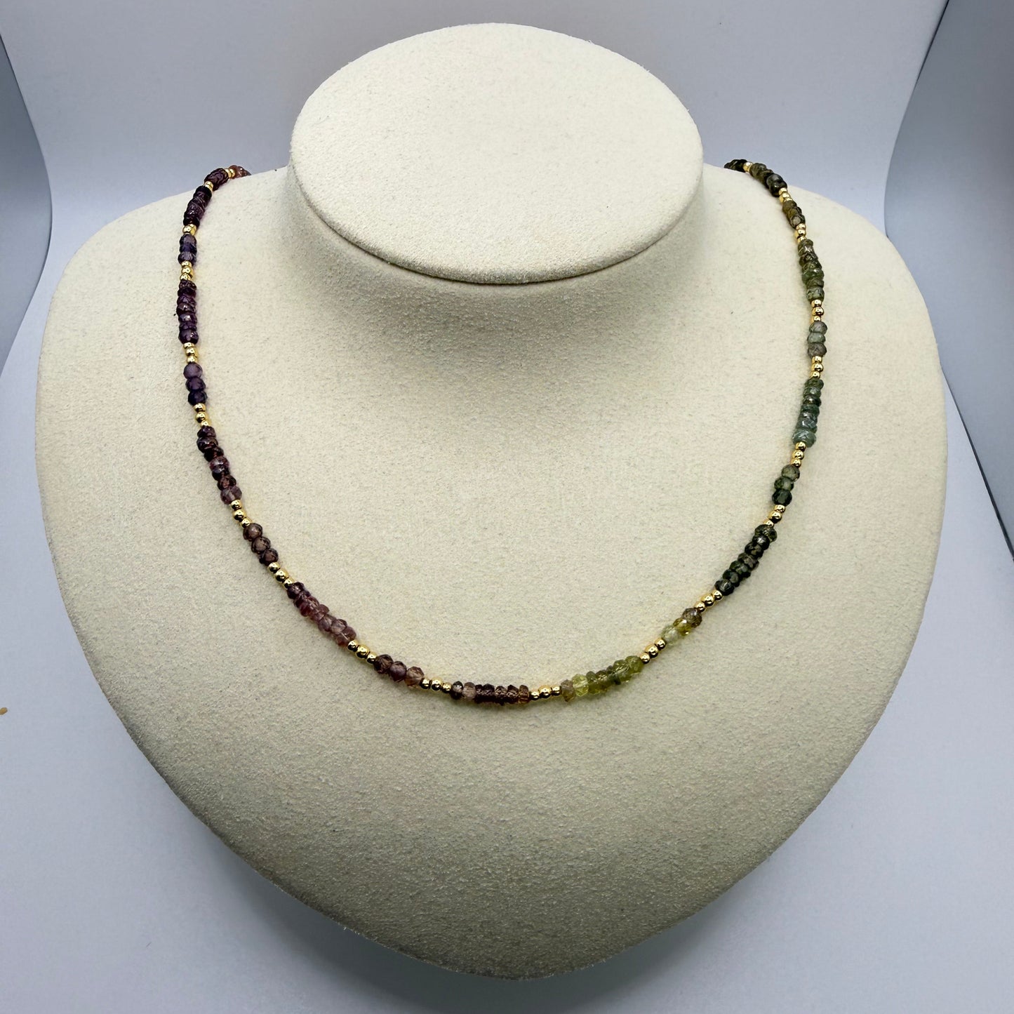 Necklace with green and purple beads on a textured beige display bust. 