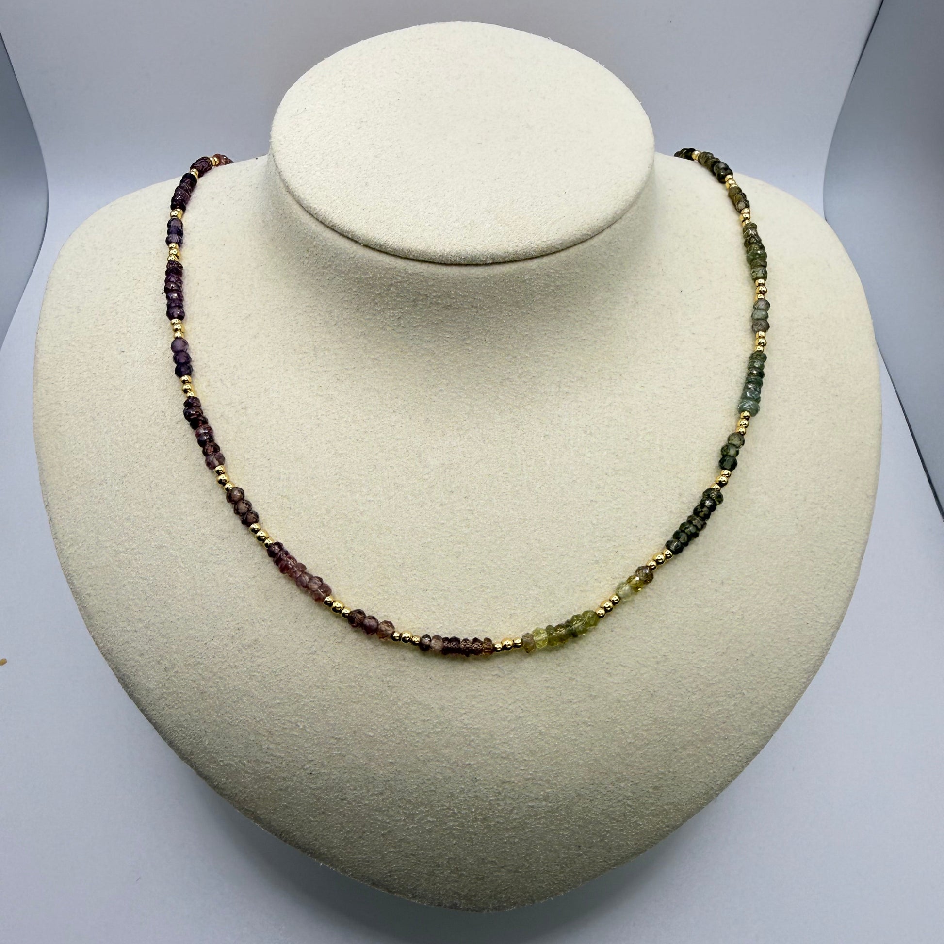 Necklace with green and purple beads on a textured beige display bust. 