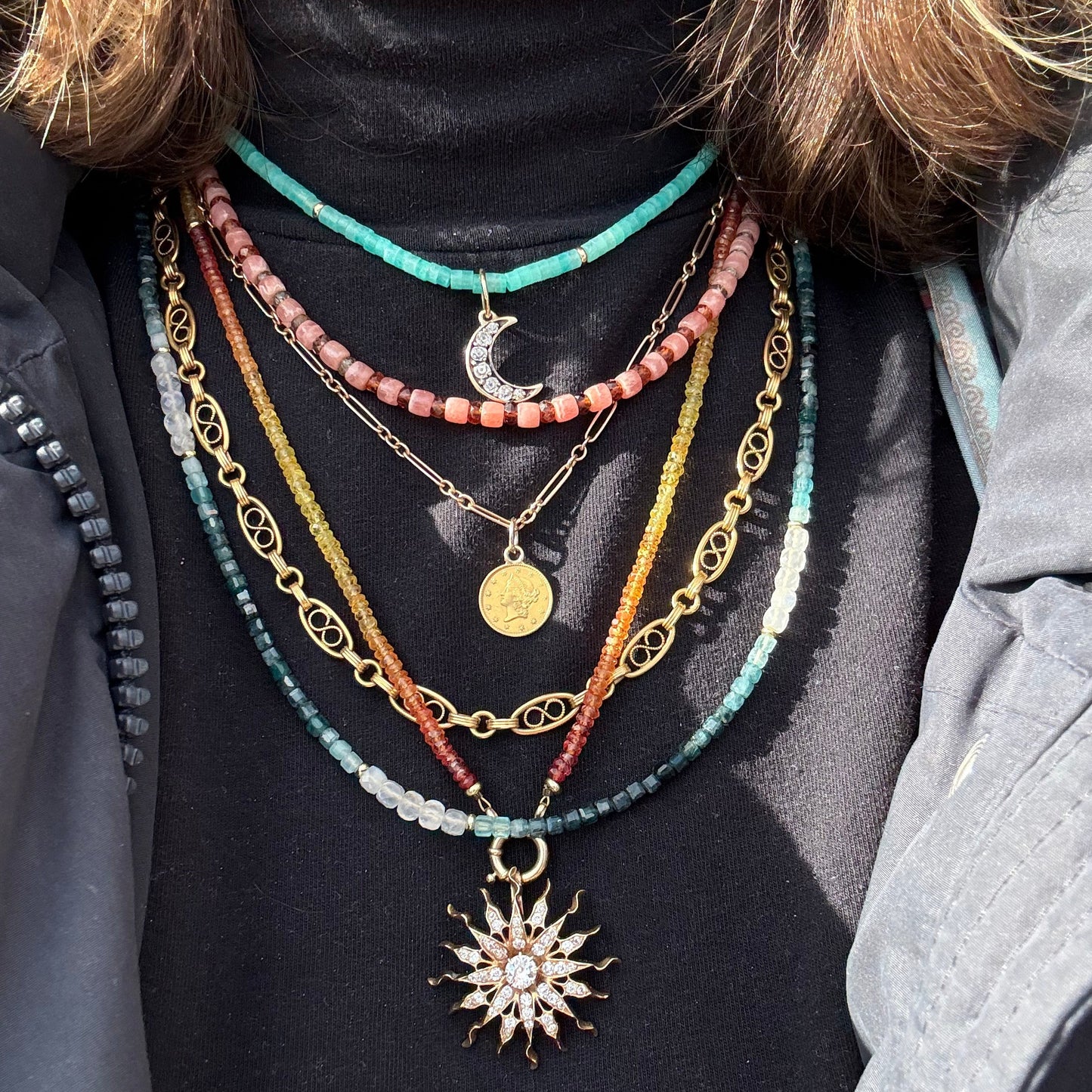 Close-up of a person wearing multiple necklaces with various pendants on a dark surface.