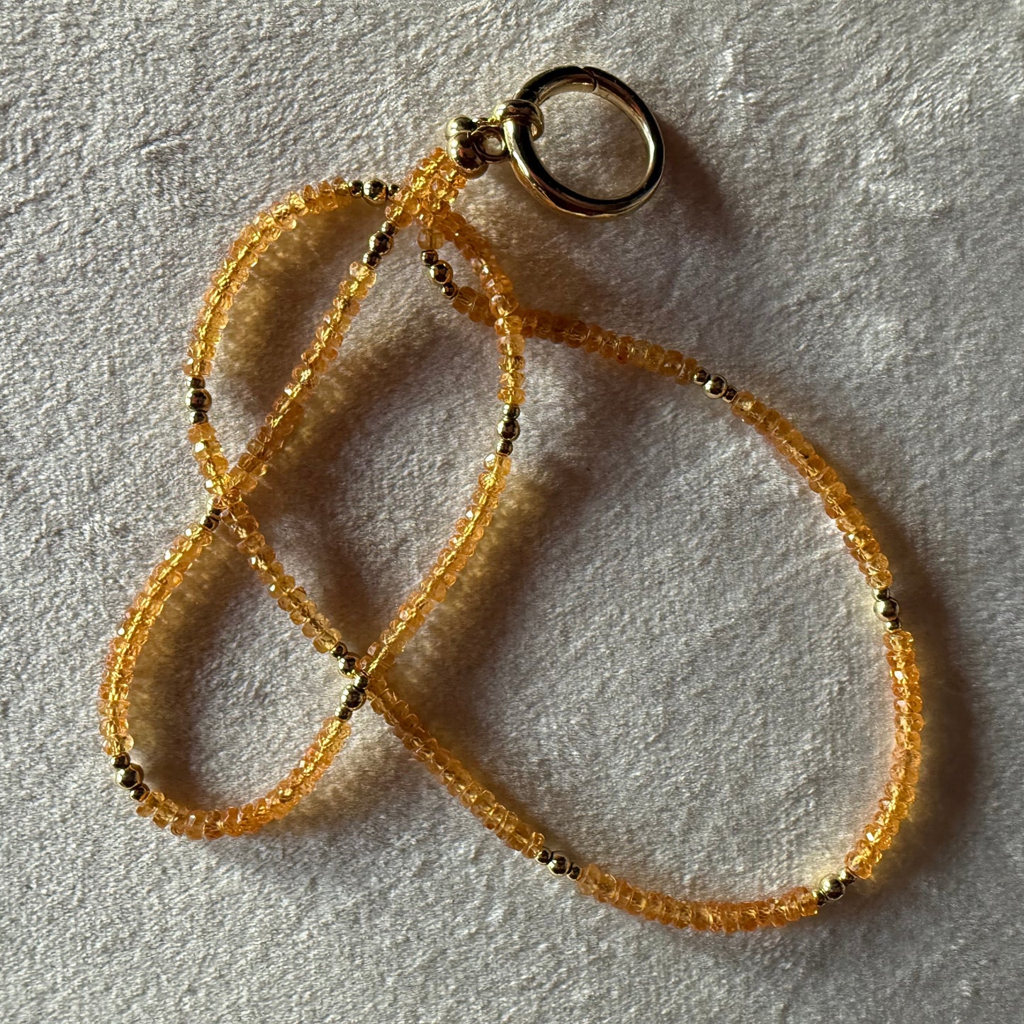 Gold and orange beaded necklace on a textured light surface