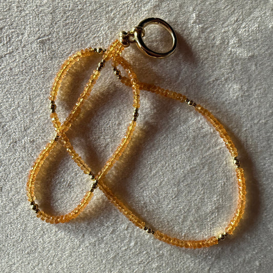 Gold and orange beaded necklace on a textured light surface