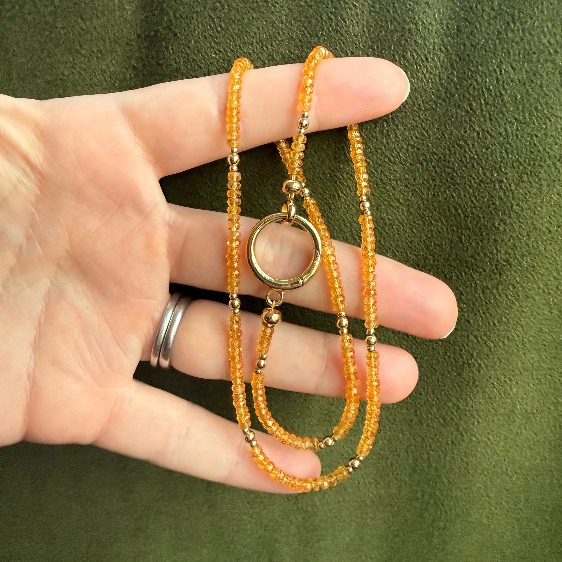 Hand holding an orange beaded necklaces against a green background