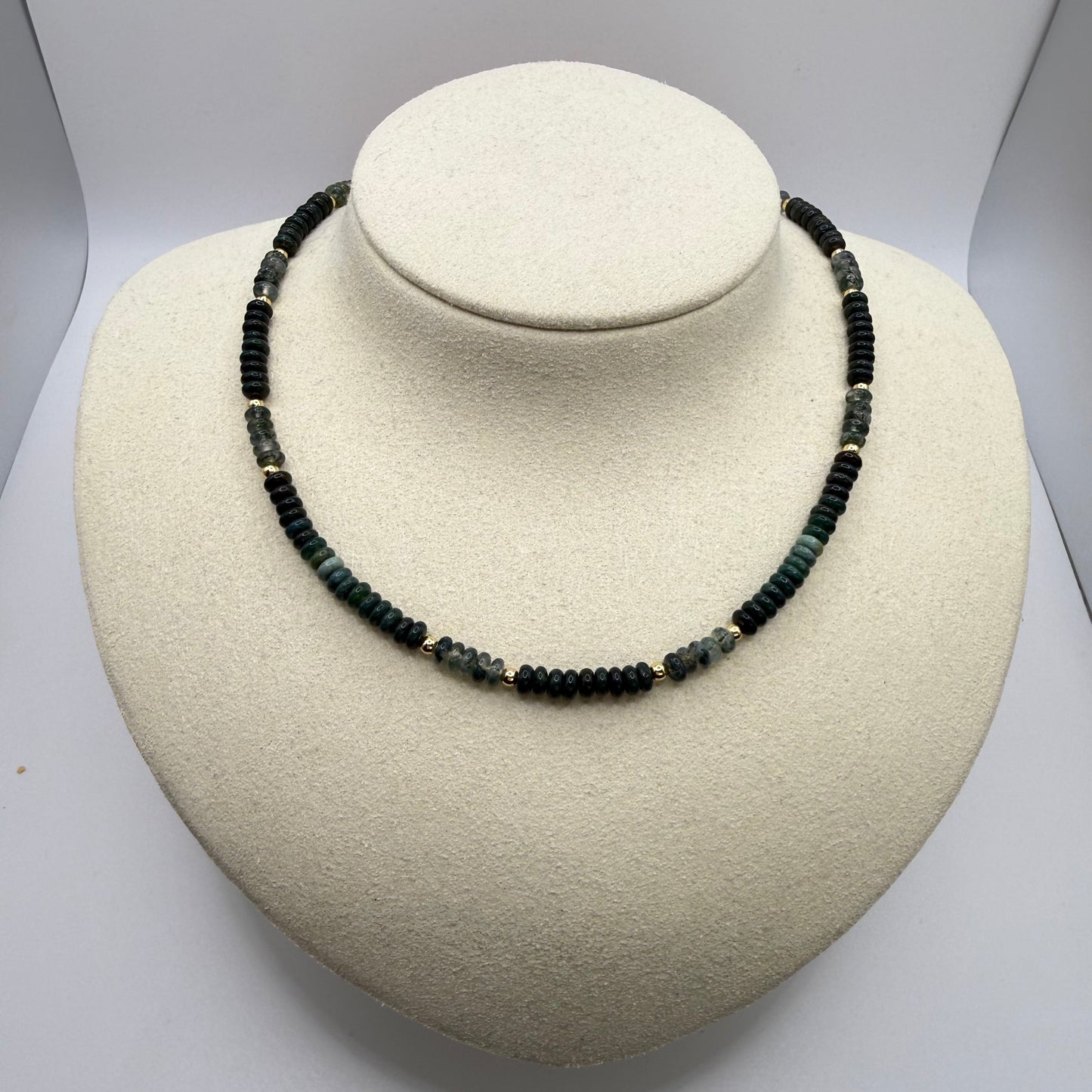 Necklace with green beads on a white display bust.