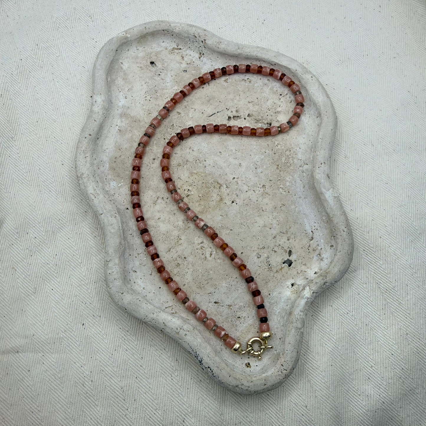 Necklace with pink and earth toned beads on a textured beige surface