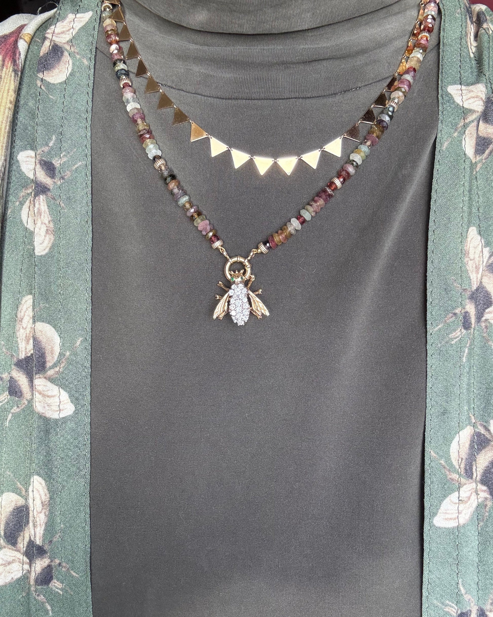 Beaded necklace with bee charm on a floral-patterned fabric background