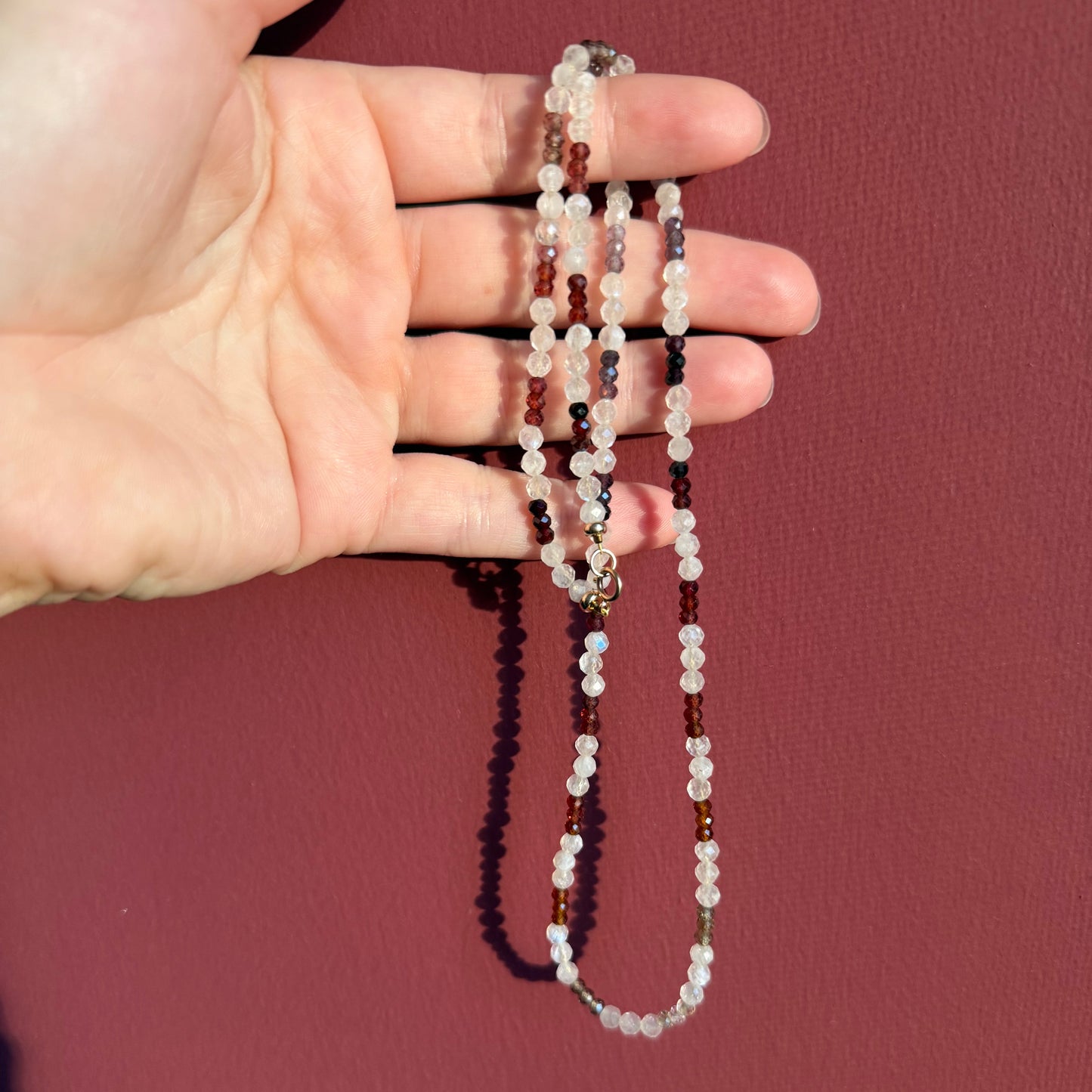 Hand holding a beaded necklace against a dark plain background
